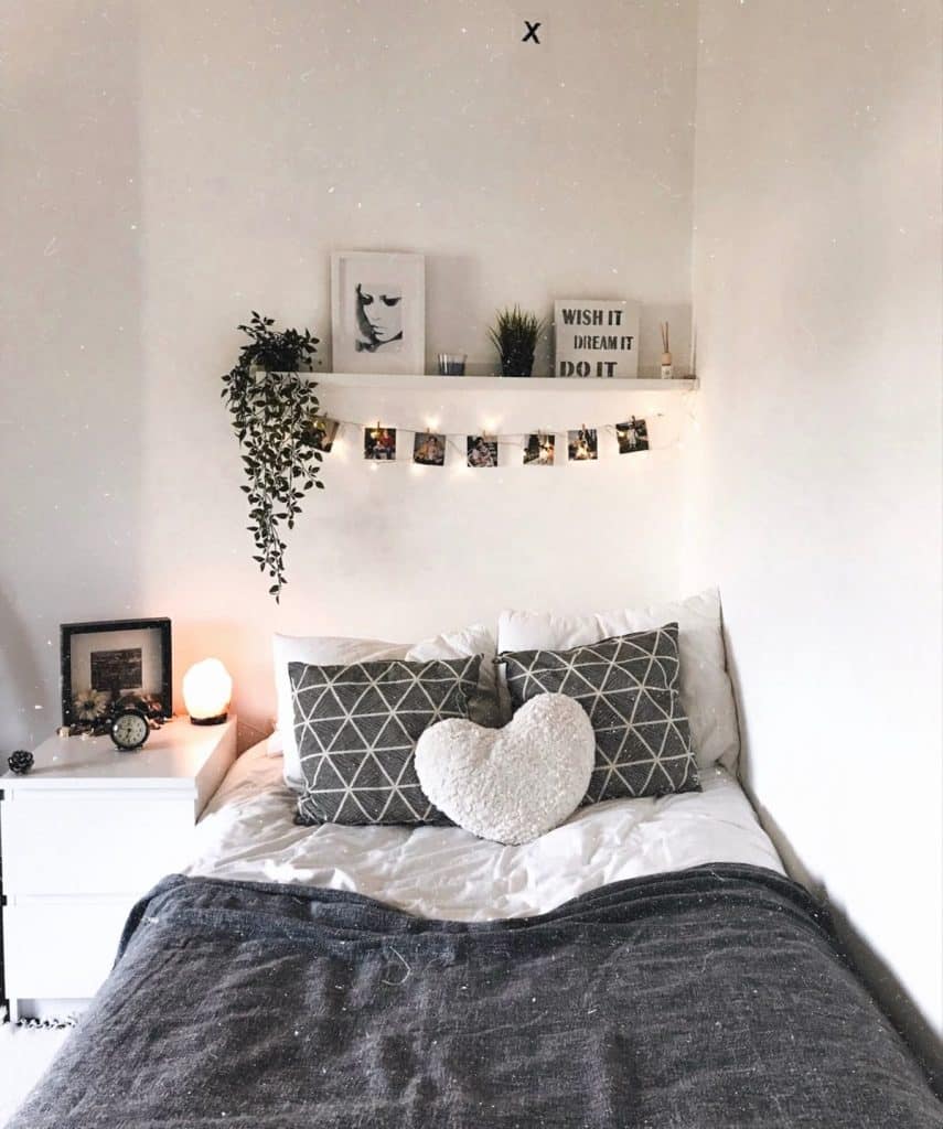 A row of polaroid photos hangs from clothespins beneath a white floating shelf strung with fairy lights.