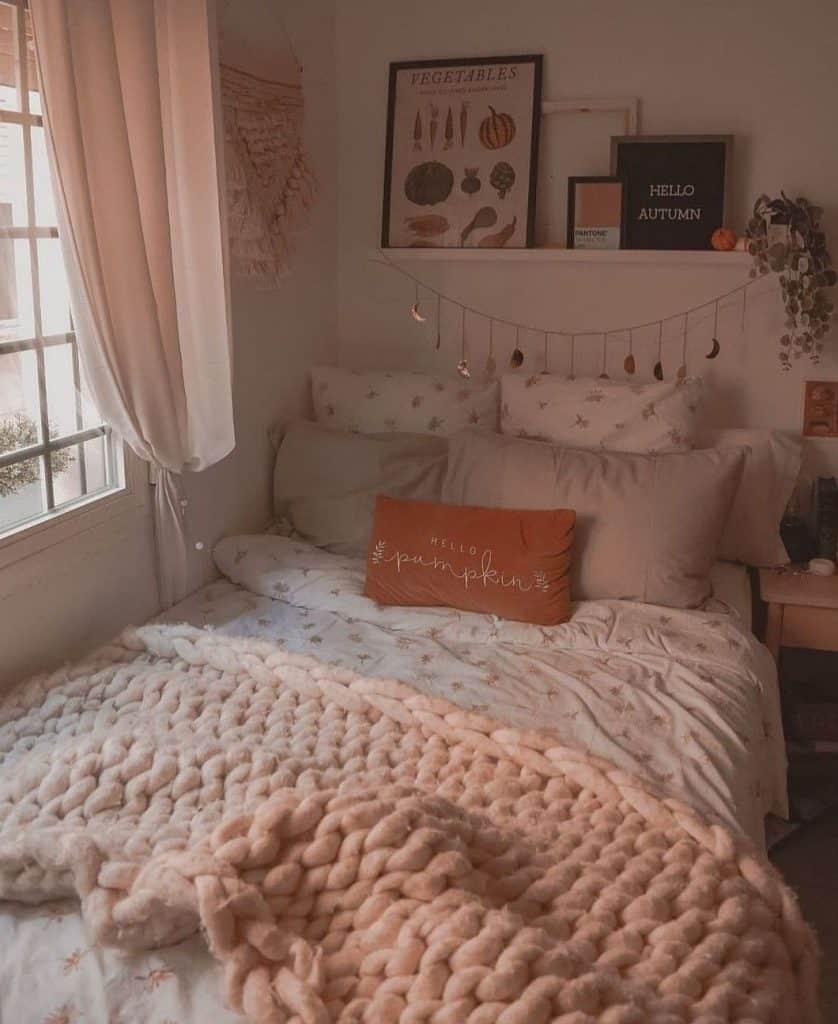An orange Hello Pumpkin throw pillow sits against neutral bedding beneath a shelf styled with an autumn sign.