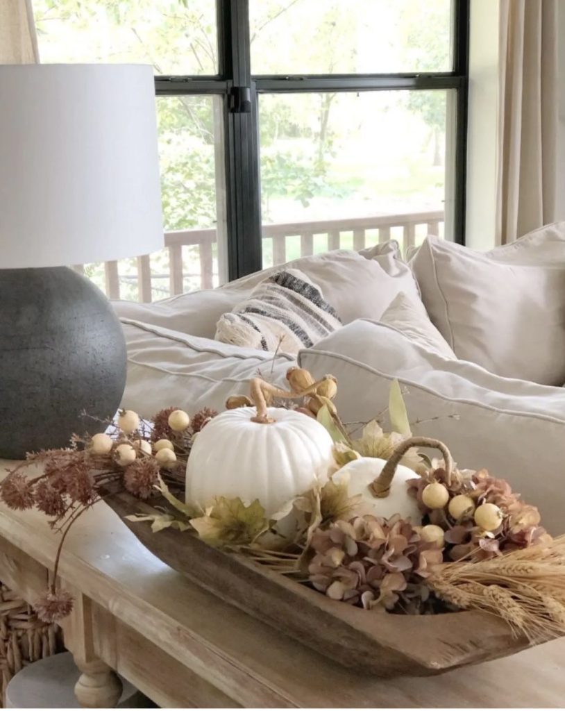 Muted neutral fall dough bowl on a console with two white pumpkins, dried brown hydrangea, wheat, cream berries, and dried grasses.