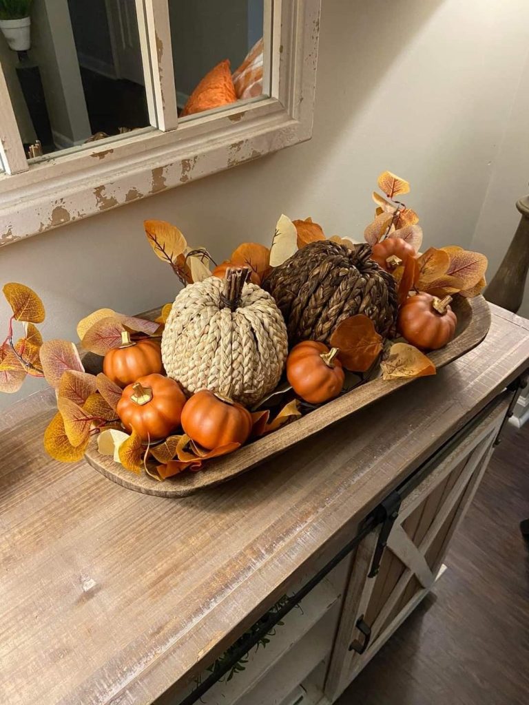 Rustic fall dough bowl on a wood console with two woven seagrass pumpkins, orange mini pumpkins, and orange and purple eucalyptus leaves.