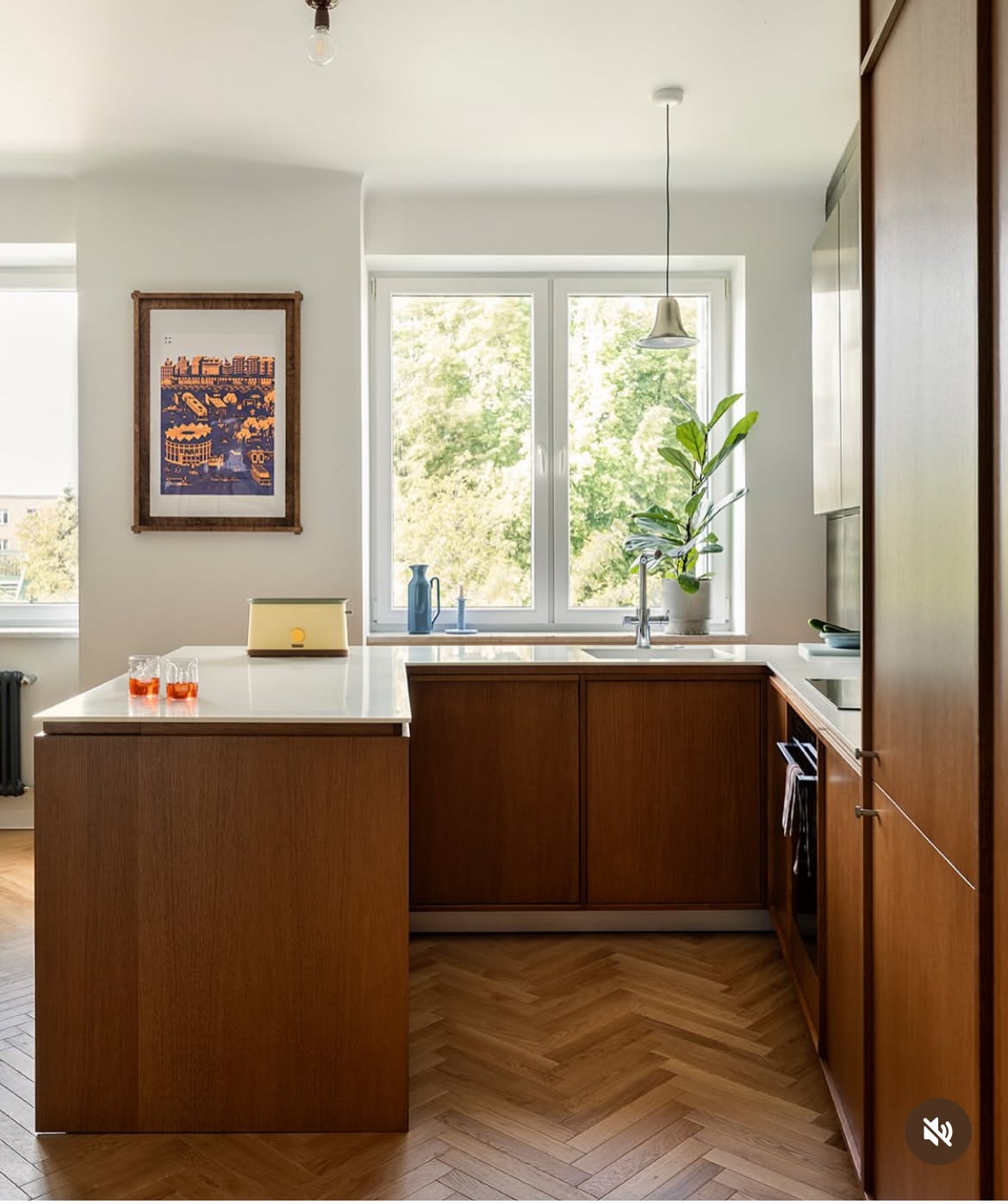Two-tone kitchen with warm orange upper cabinets, cream lower cabinets, half-moon cut-out pulls, a sage green stacked tile splashback and a curved walnut breakfast bar.