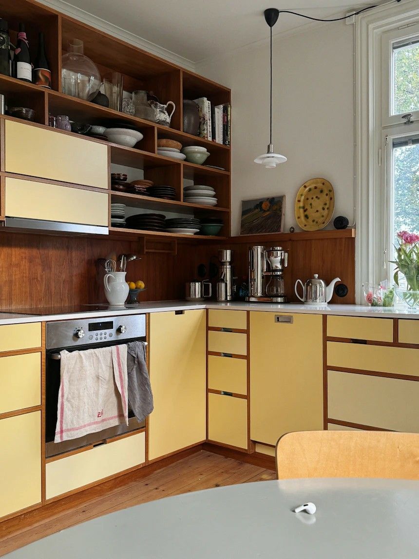 Authentic vintage kitchen with butter yellow laminate cabinet fronts trimmed in teak, an open teak display hutch, a white benchtop and a white pendant light.
