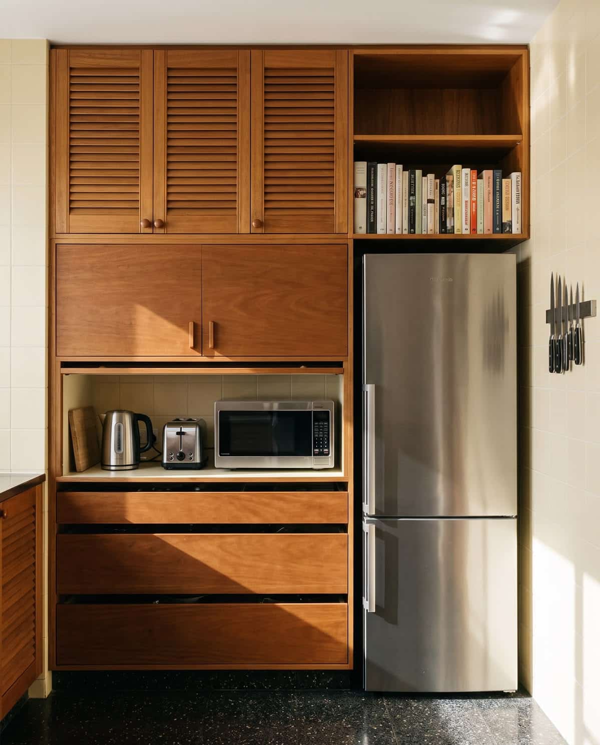Floor-to-ceiling timber kitchen joinery with louvred cabinet doors, an appliance garage holding a kettle and toaster, a built-in cookbook slot and an integrated fridge.