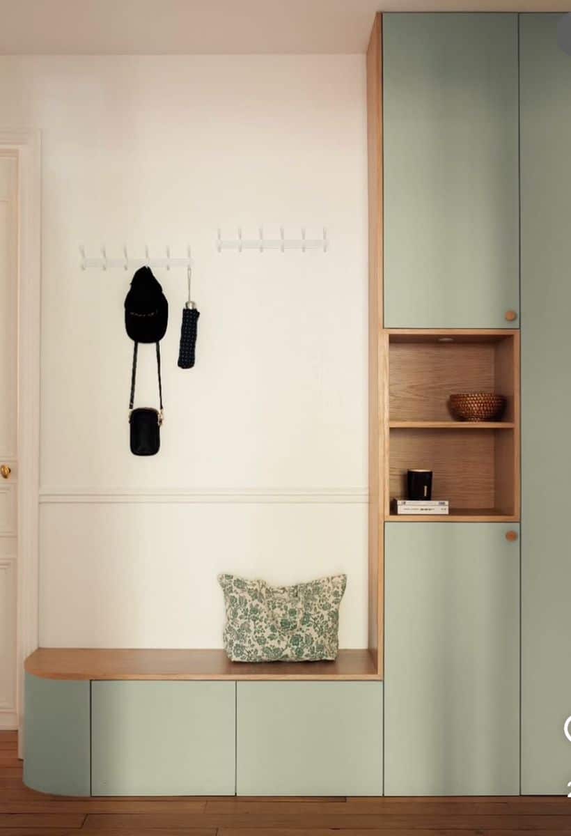 Modern entryway with sage green built-in cabinetry, a wood-topped bench with drawers, an oak-lined open niche holding a bowl and books, and white flip-down hook rails on the wall above.