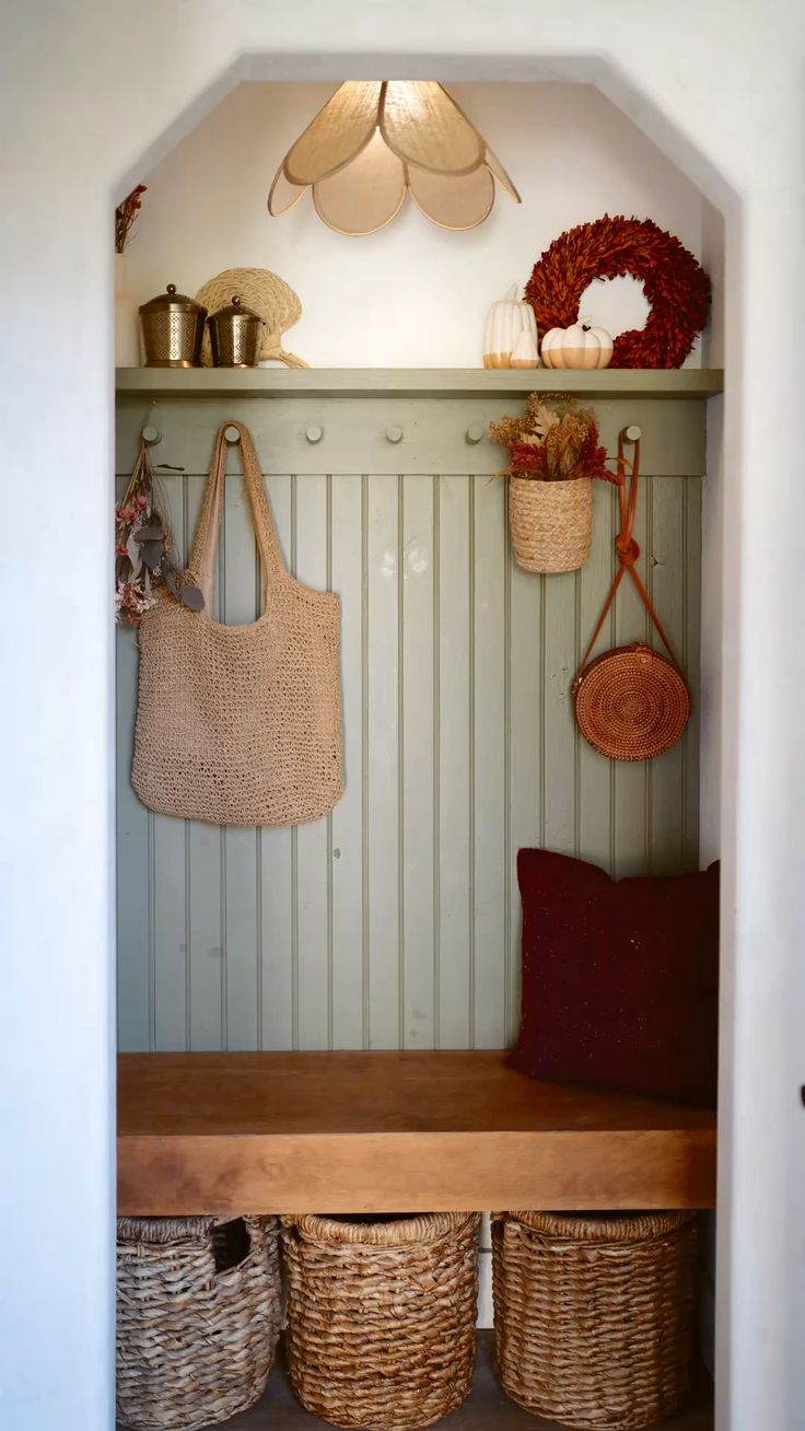 Arched entry nook with sage green beadboard, a white Shaker peg rail holding woven bags, a scalloped rattan pendant light, autumn styling on the shelf, and a wood bench over three woven baskets.