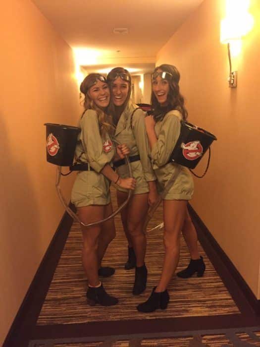 Three people dressed as Ghostbusters in tan boiler suits with goggles and proton packs made from painted buckets and hoses.